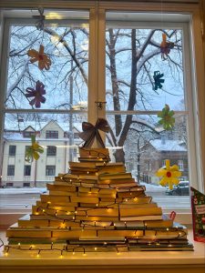 Raamatutest püramiid mis on jõulutuledega kaunistatud. Taustal vaade aknast lumisesse hoovi.
